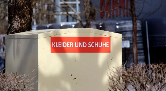 Ein weißer Container auf der Straße. Auf einem roten Streifen steht in weißer Schrift Kleider und Schuhe.