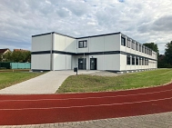 Ein zweigeschossiger Container auf einem Rasenplatz. Im Vordergrund ist eine rote Laufbahn zu erkennen. © Landkreis Rotenburg (Wümme)