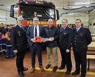 Fünf Männer, drei davon in Feuerwehruniform stehen vor einem roten Feuerwehrauto und halten einen großen roten Schlüssel in die Hand. Im Hintergrund stehen Mitglieder der Jugendfeuerwehr in neonfarbenen Jacken. © Landkreis Rotenburg (Wümme)